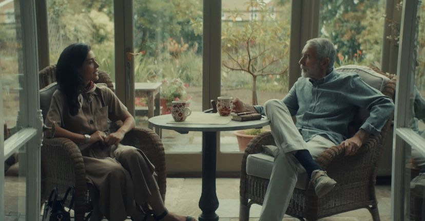 Heléna Antonio, wearing a pale beige dress, sits opposite Syed Massood, wearing a pale blue shirt and white trousers.