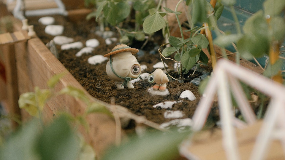 Still from Marcel the Shell with Shoes on, with Marcel and Connie stood in their leafy garden.