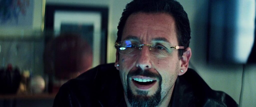 A euphoric Adam Sandler, wearing glasses in his jewellers office.